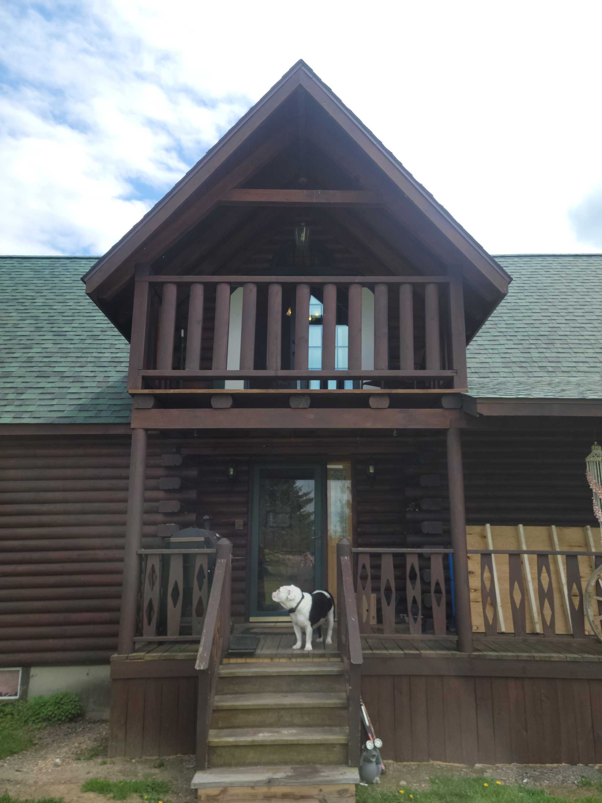 Log cabin with dog on wooden stairs.