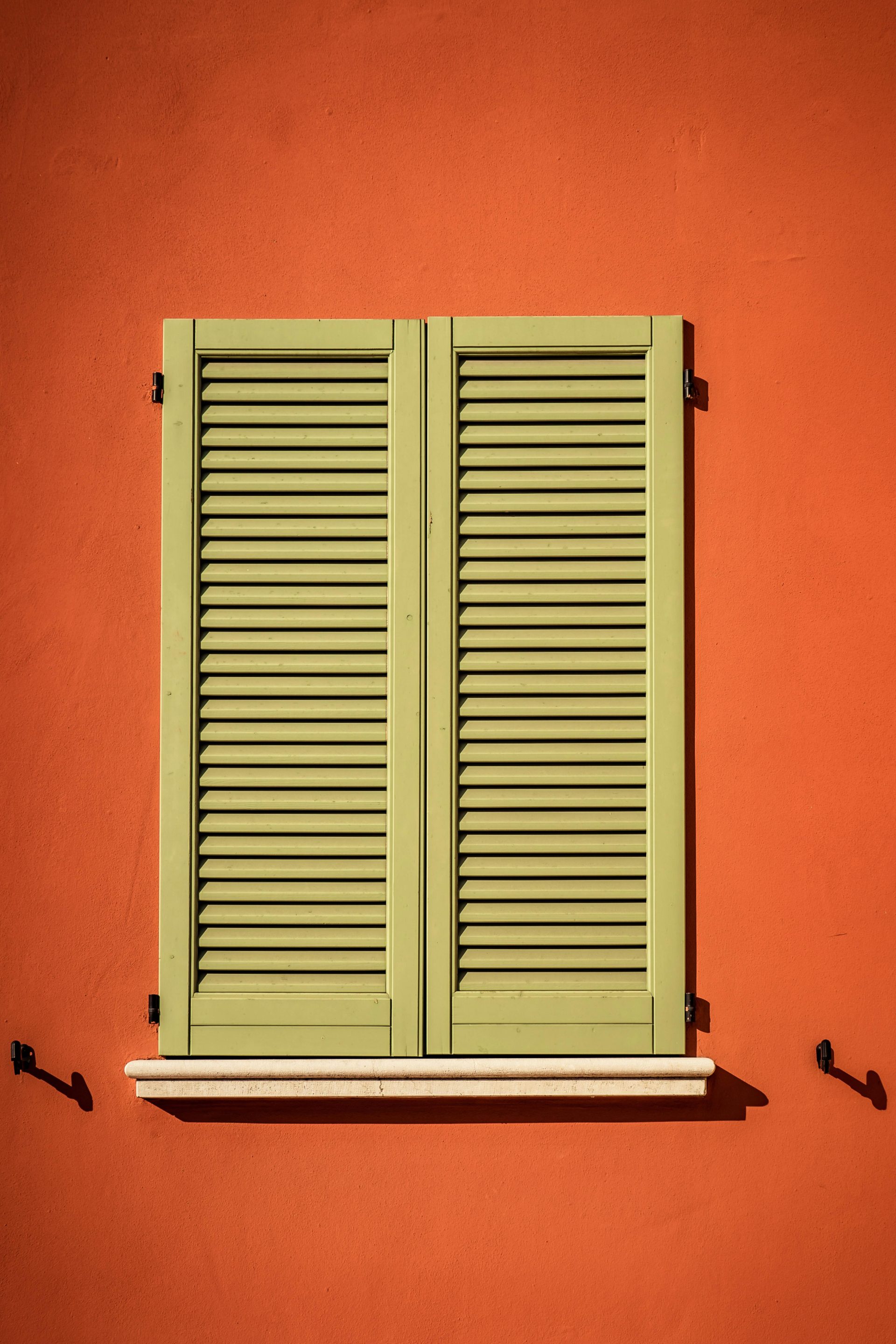 A vintage green shuttered window on a vibrant orange wall captures architectural charm.